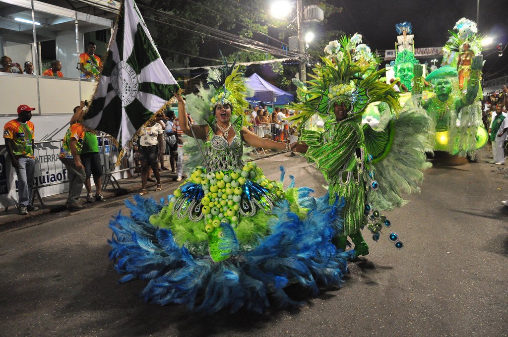 A passista in a green and blue feathered costume dancing during a Rio Carnival parade